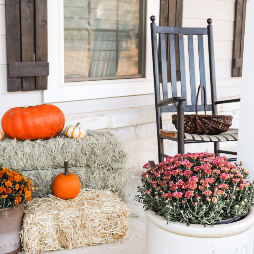 Fall outdoor décor mums rocking chair basket pumpkins and hay bales.